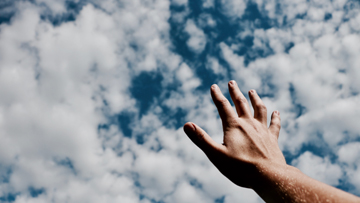 Hand reaching hopefully for a beautiful cloud-filled sky