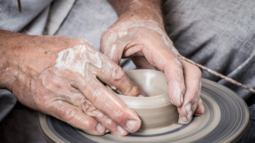 Hands working to shape clay on a potter's wheel